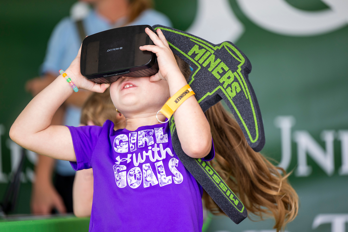 Girl looking at a virtual reality headset with a Miner pickaxe at the State Fair.